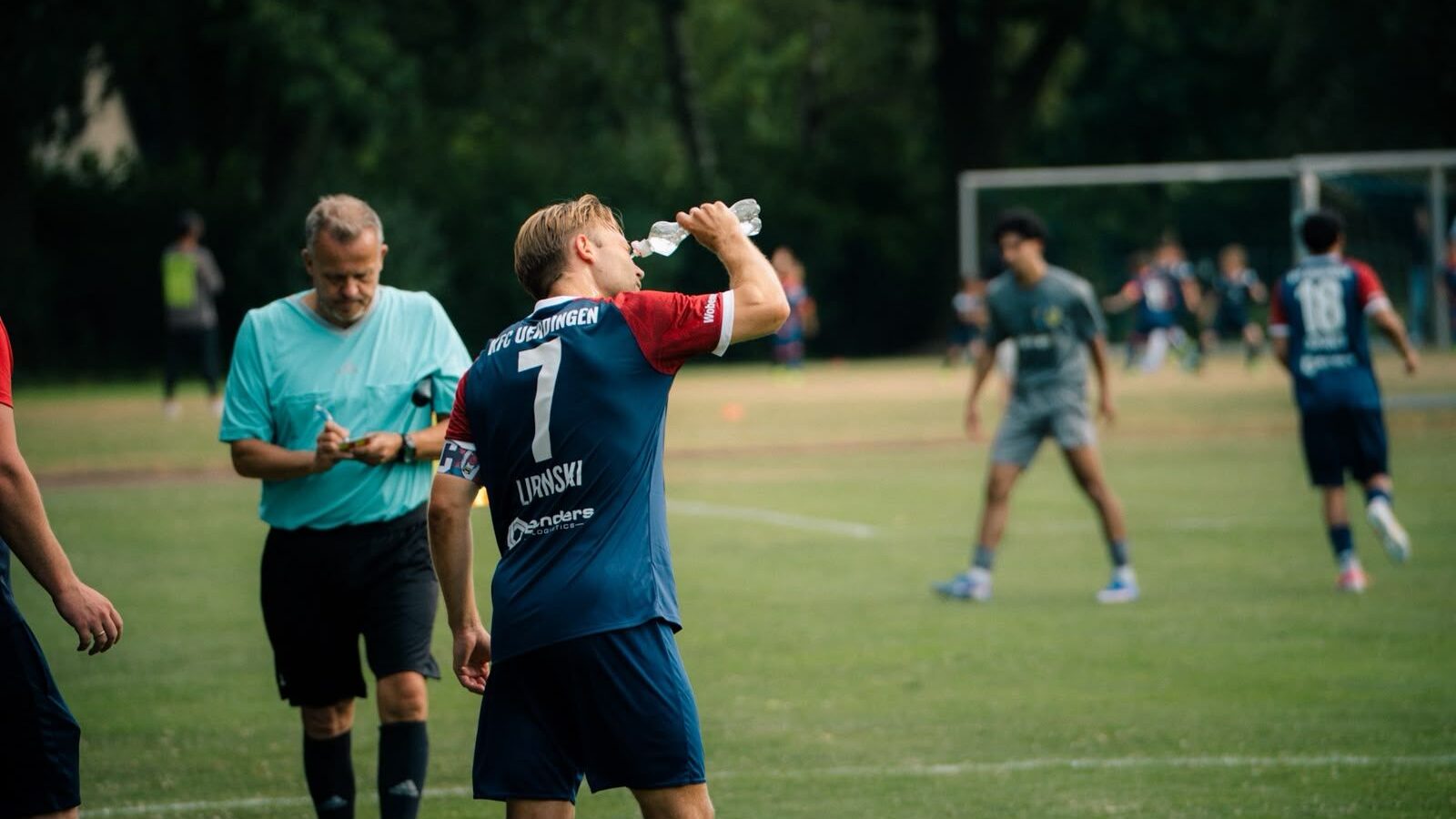 KFC-Spieler in Blau-Rot am Spielfeldrand, im Hintergrund läuft das Spiel